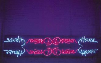 A dark purple room with a neon sign in loose handwriting that says 