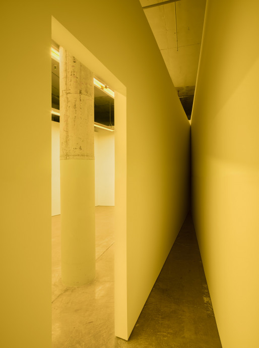 A doorway frames a column and two walls intersecting at a narrow angle, all bathed in yellow fluorescent light.