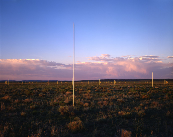 Tall silver poles sticking up out of a grassy landscape, with purple storm clouds in the sky.
